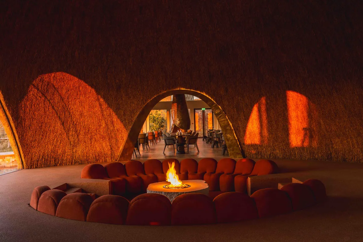 A sunken lounge of curved velvet seating around an open fire