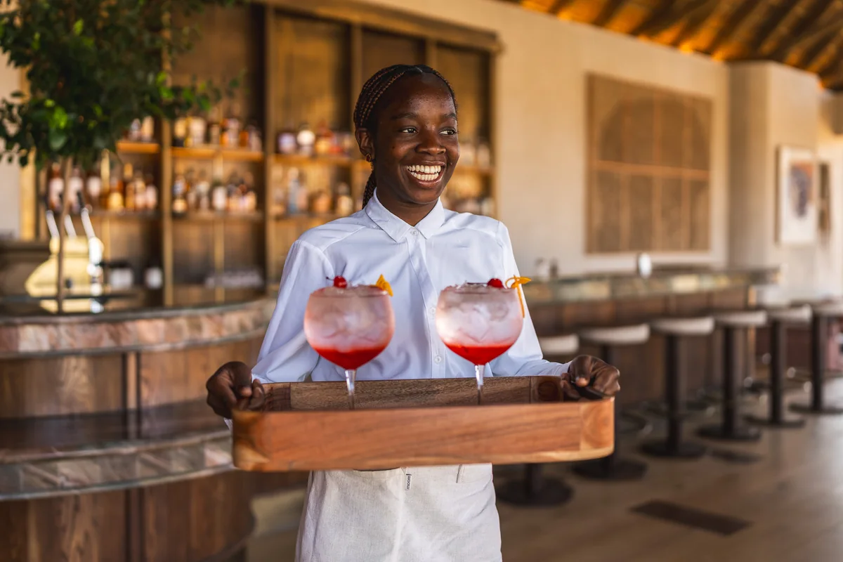 A smiling host carrying sundowners on a tray